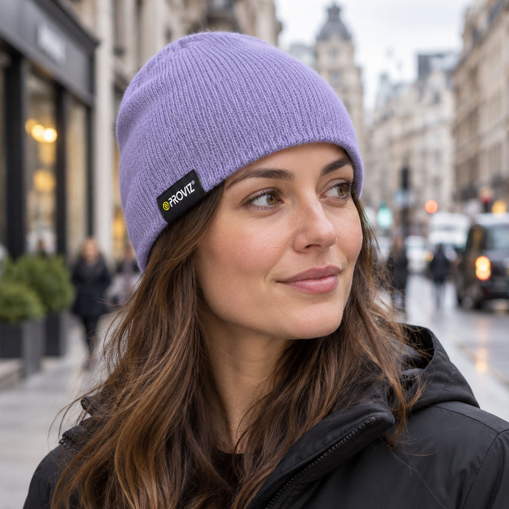 lifestyle A woman wearing a lavender purple ribbed knit beanie with a black and yellow PROVIZ logo patch, photographed outdoors on a city street.