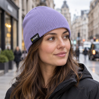 lifestyle A woman wearing a lavender purple ribbed knit beanie with a black and yellow PROVIZ logo patch, photographed outdoors on a city street.