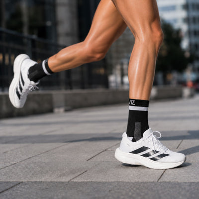 lifestyle A person running outdoors wearing white Adidas sneakers with Proviz black stripes and black crew socks with white stripes and a visible Adidas logo.