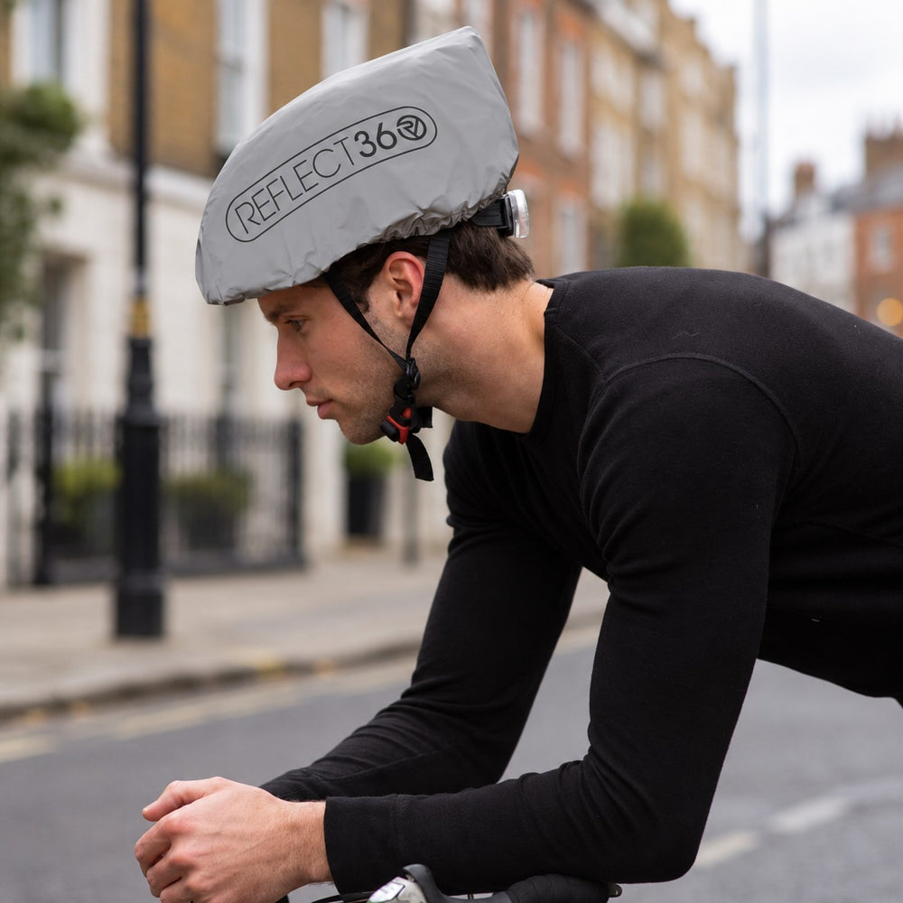 lifestyle A man wearing a black long-sleeve cycling jersey and a reflective silver-gray Proviz helmet cover with the brand name 'REFLECT360' riding on a city street.