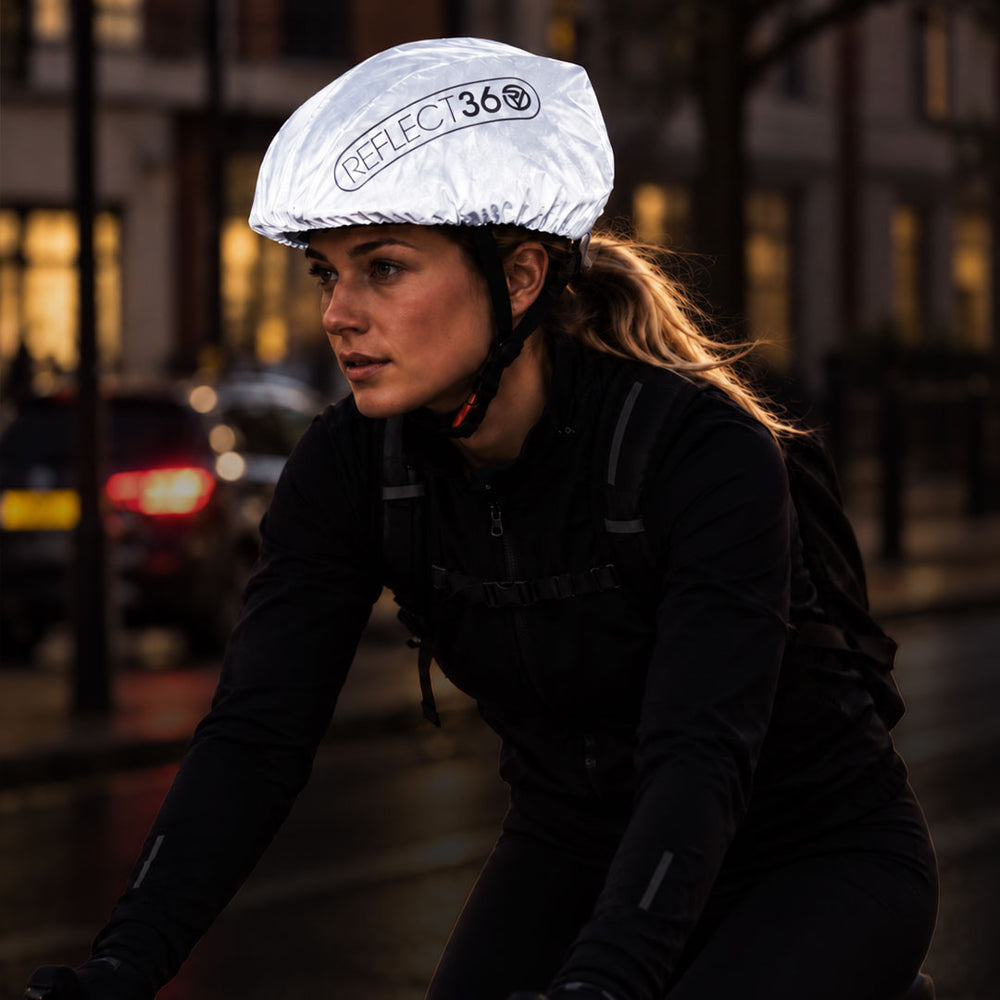 lifestyle A cyclist wearing a reflective silver proviz helmet cover with the brand name 'REFLECT360' printed on it, riding on a city street at night.