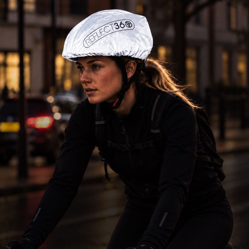 lifestyle A cyclist wearing a reflective silver proviz helmet cover with the brand name 'REFLECT360' printed on it, riding on a city street at night.