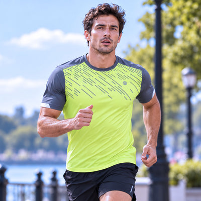 lifestyle A man running outdoors wearing a bright neon yellow-green athletic proviz lightweight t-shirt with dark gray sleeves and a diagonal stripe reflective pattern on the chest, paired with black shorts.