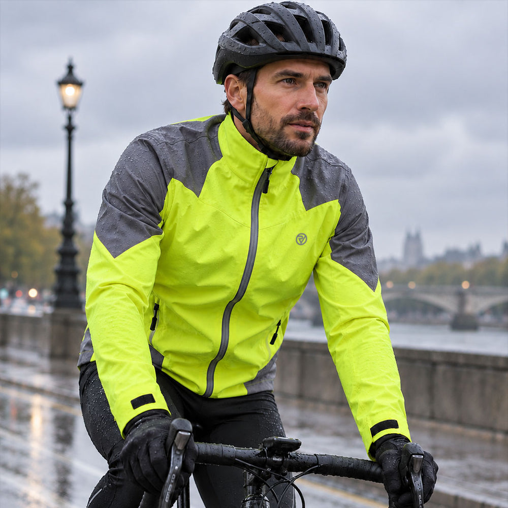 lifestyle A man wearing a bright proviz neon yellow and gray cycling jacket, black helmet, and black gloves rides a bicycle on a wet city street by the river.