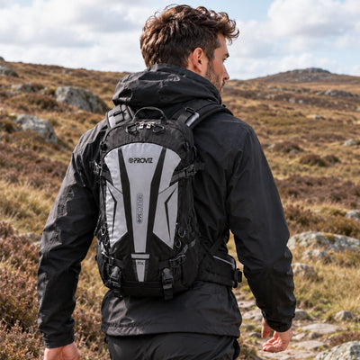 lifestyle A man hiking outdoors on a rocky, grassy mountain path, viewed from behind as he wears a black and gray Proviz 20L touring backpack.
