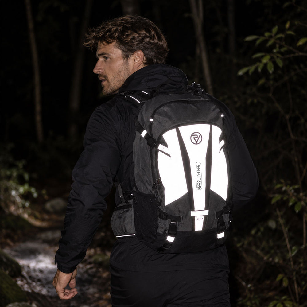 lifestyle A man hiking in a dark forest wearing a black and white reflective backpack with the brand name 'proviz' visible on the back panel.