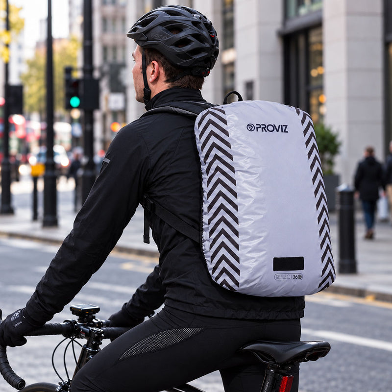 lifestyle A reflect360 backpack cover with a light gray body, black chevron patterns on the sides, and a light loop at the bottom in the city during the day