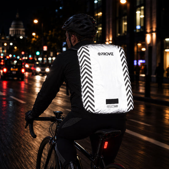 listing-lifestyle A Proviz reflect360 backpack cover with a light gray body, black chevron patterns on the sides, and a light loop at the bottom at night in city