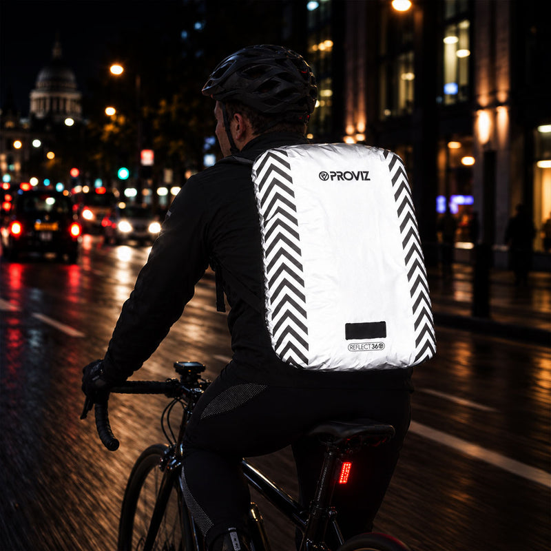 listing-lifestyle A Proviz reflect360 backpack cover with a light gray body, black chevron patterns on the sides, and a light loop at the bottom at night in city