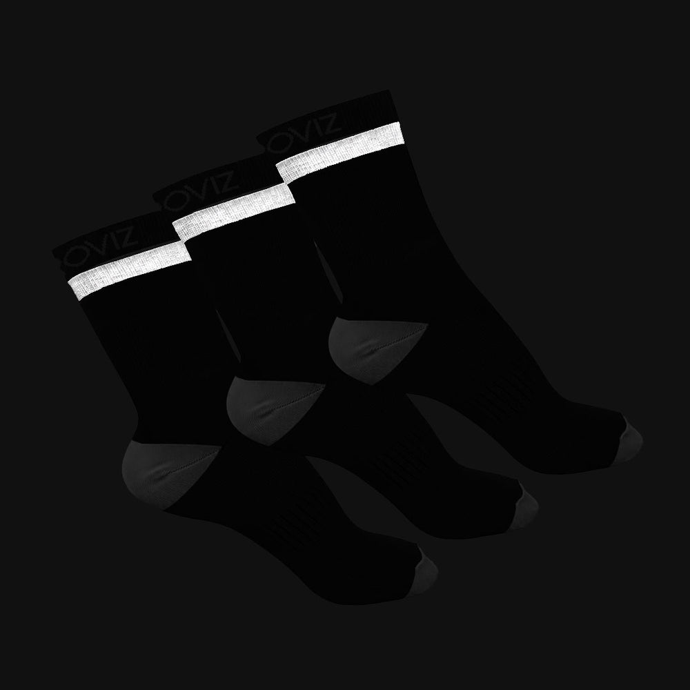 Three black crew socks with white reflective-looking bands at the top and gray heel/toe accents, arranged on a dark background. The cuff shows the brand name PROVIZ.