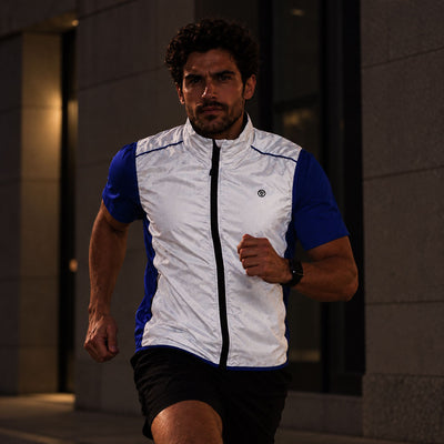 lifestyle A man running outdoors at night wearing a reflective and blue athletic zip-up vest with black shorts.