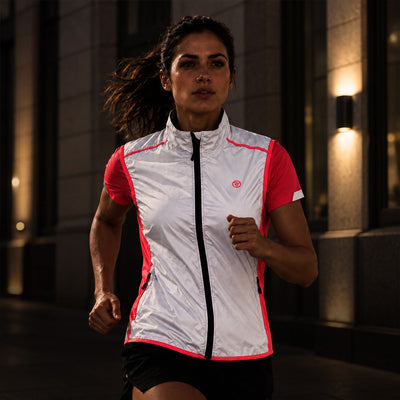 lifestyle A woman running outdoors at night wearing a Proviz reflective, white and pink athletic vest with a black zipper. The vest has a small circular logo on the left chest.