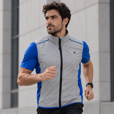 lifestyle A man running outdoors wearing a Proviz light gray reflective and blue athletic zip-up vest over a blue shirt, with a modern stone building in the background.