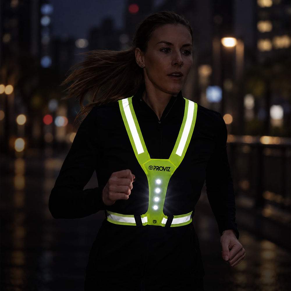 lifestyle A woman running at night wearing a bright neon yellow reflective vest with integrated LED lights. The vest features the brand name 'PROVIZ' printed on the front.