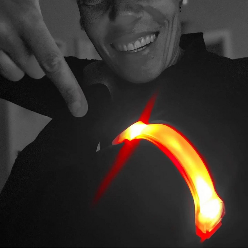 lifestyle A close-up black and white photo of a smiling woman pointing toward a glowing orange-red curved Proviz light or arrow on her chest, with her hand near her face.